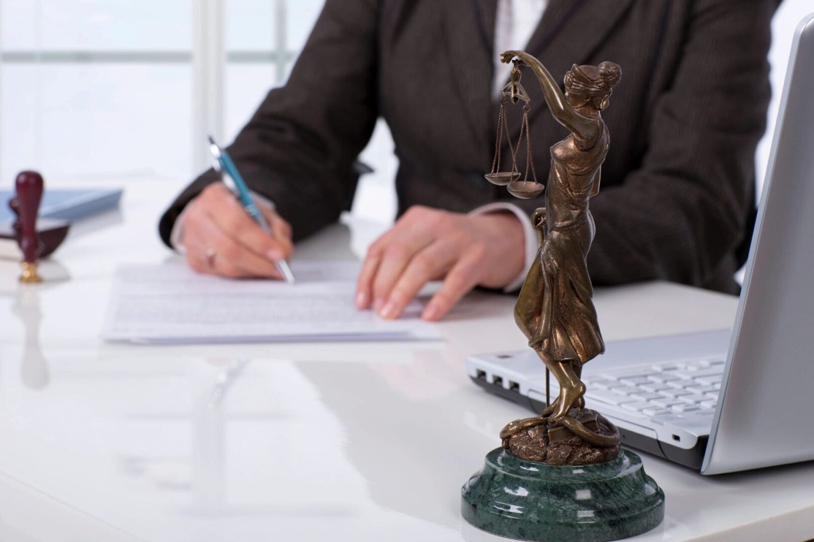 A person sitting at a desk with papers and a statue of justice.